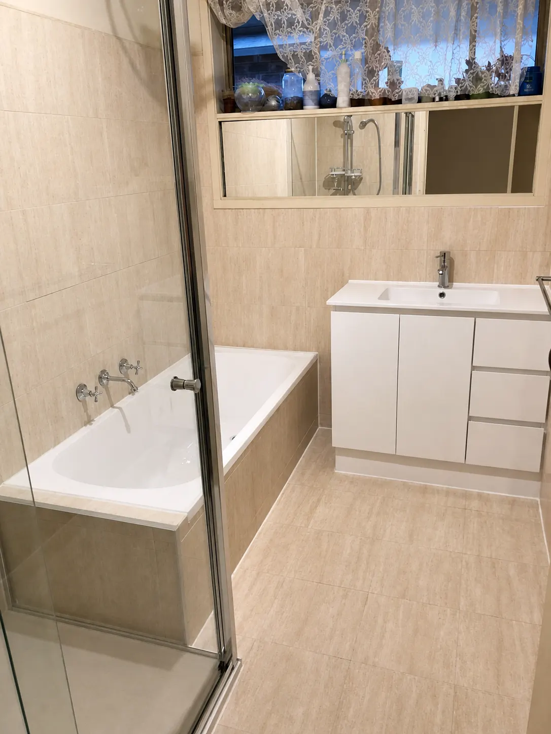 Finished warm neutral bathroom with tiled bath, glass shower screen and white vanity